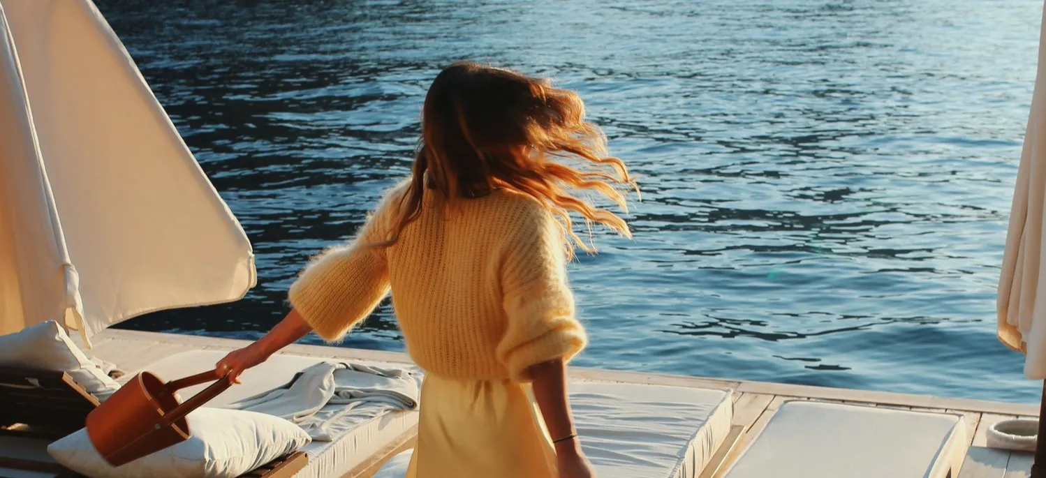 A woman in a yellow jumper beside the water